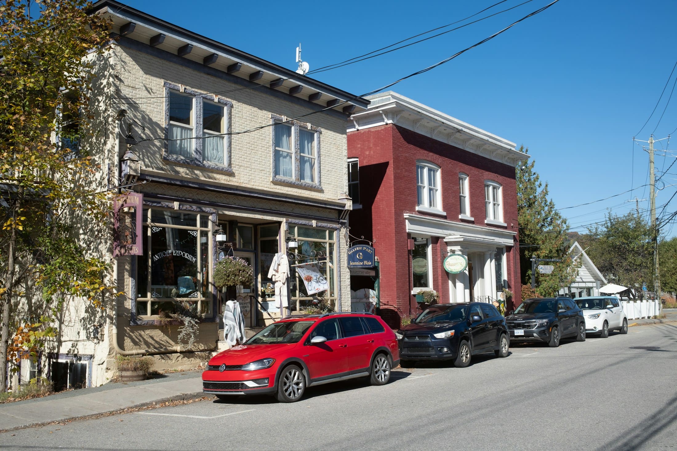 A sunny main street in North Hatley, Quebec, lined with independent shops and parked cars.